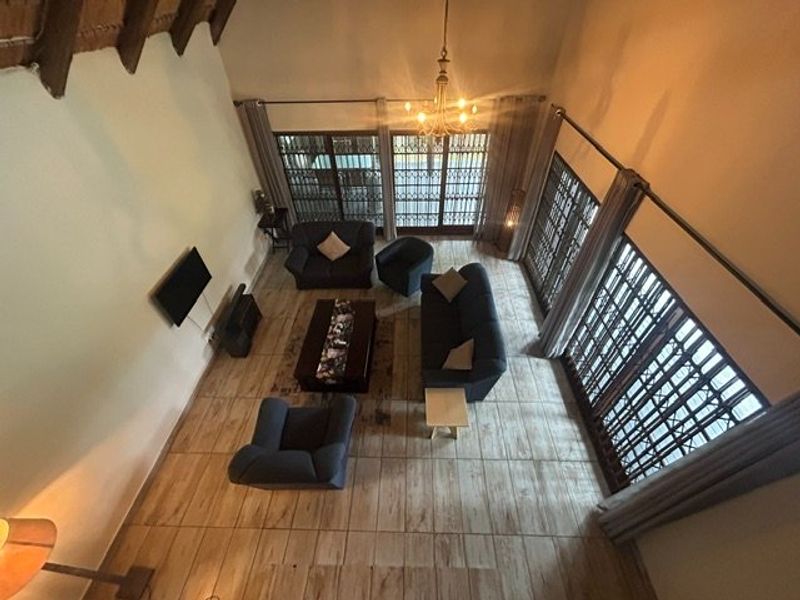 Spacious living room featuring a high vaulted ceiling with exposed timber beams, tiled flooring, and large glass doors with security gates.