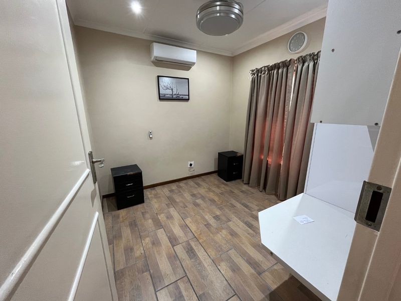A functional bedroom featuring tiled flooring, a wall-mounted air conditioning unit, and a built-in desk area.