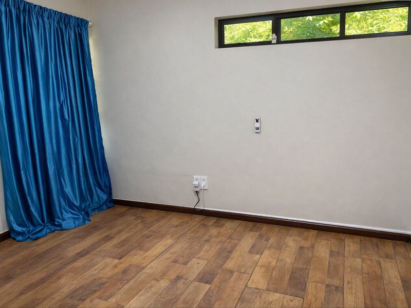 An empty bedroom featuring wood-look laminate flooring, neutral walls, and a high-set horizontal window providing natural light.