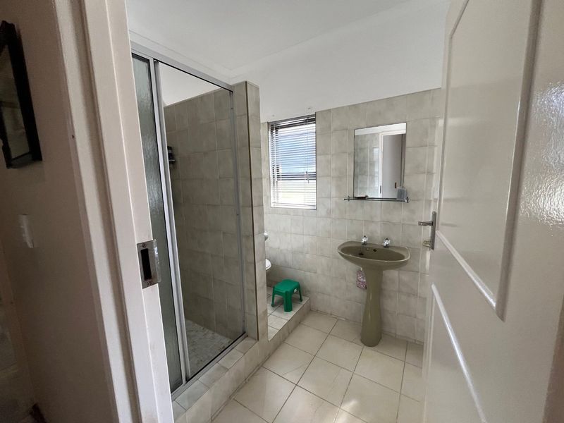 A functional bathroom featuring a tiled shower enclosure, pedestal basin, and neutral wall tiling, offering a clean and practical layout.