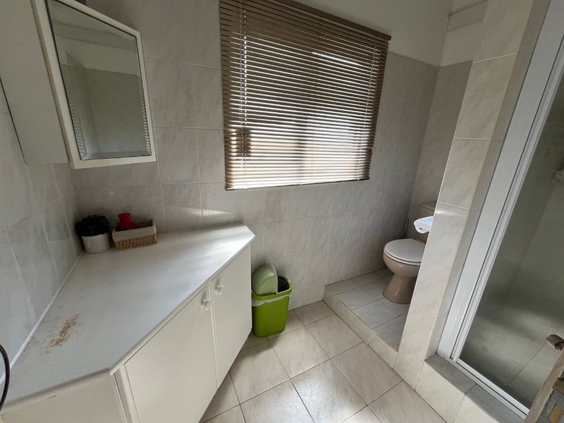A functional bathroom featuring a built-in vanity, tiled walls and floors, a separate toilet area, and a shower enclosure.