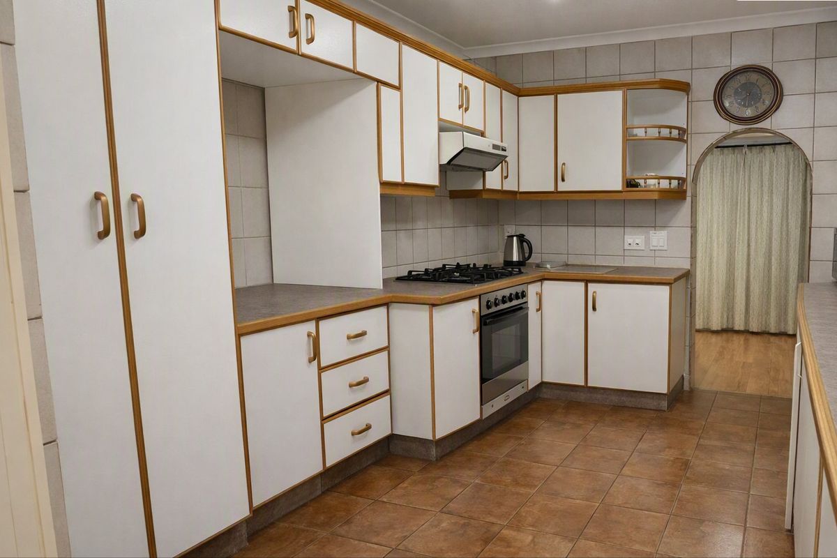 A functional kitchen featuring white cabinetry with wood trim, a gas hob, built-in oven, extractor fan, and tiled finishes throughout.
