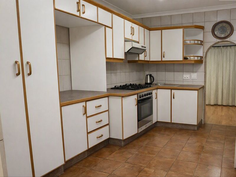 A functional kitchen featuring white cabinetry with wood trim, a gas hob, built-in oven, extractor fan, and tiled finishes throughout.