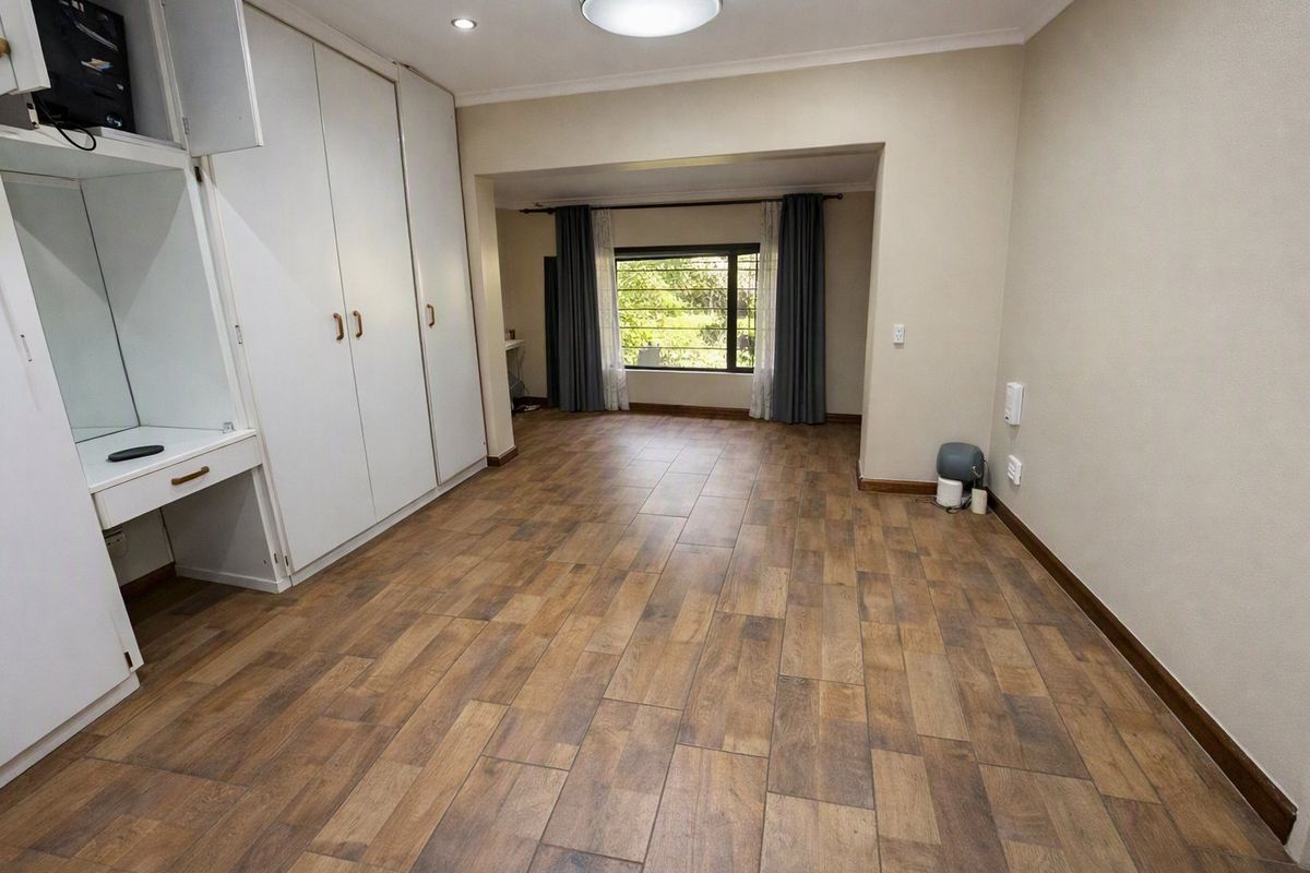 Spacious bedroom featuring wood-look tile flooring, extensive built-in cupboards with an integrated vanity, and large windows providing natural light.