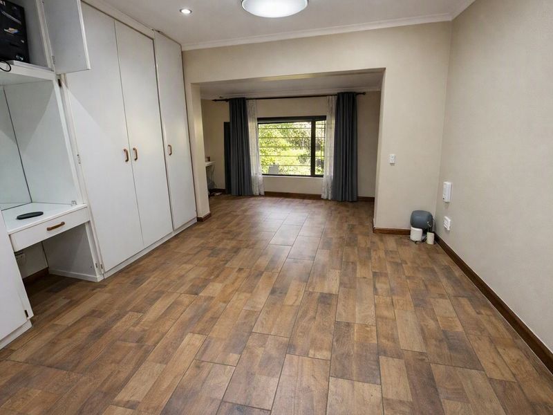 Spacious bedroom featuring wood-look tile flooring, extensive built-in cupboards with an integrated vanity, and large windows providing natural light.