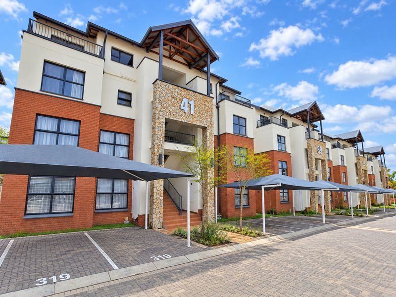 Modern apartment complex exterior featuring brick and stone facade, covered parking bays, and private balconies under a clear blue sky.