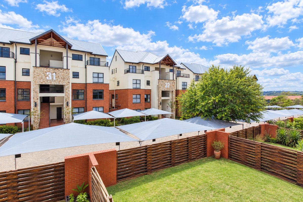 Exterior view of a multi-story apartment complex featuring brick and stone facades, metal roofing, and dedicated shade-covered parking areas with a private lawn.
