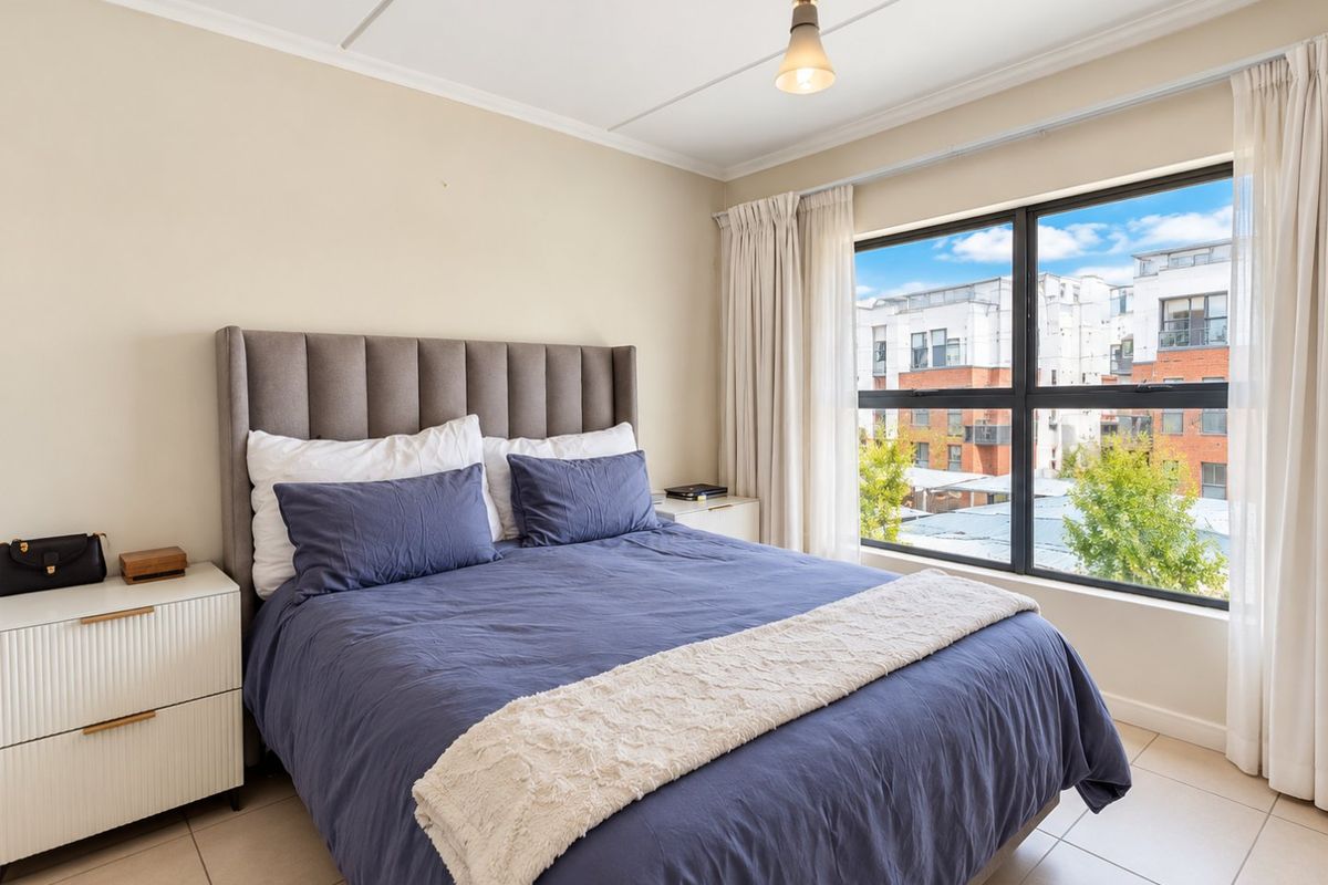 A well-lit bedroom featuring large windows with views, neutral wall tones, and tiled flooring, providing a comfortable and bright living space.