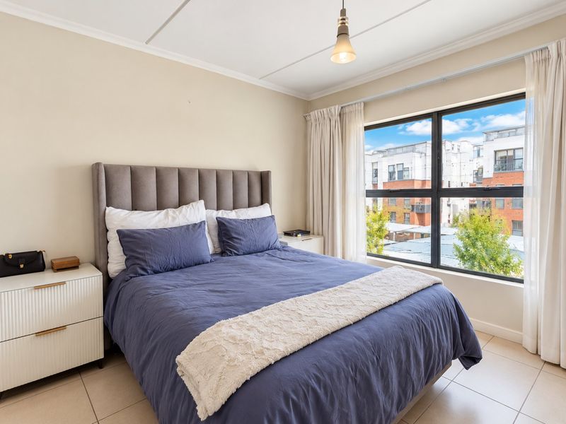 A well-lit bedroom featuring large windows with views, neutral wall tones, and tiled flooring, providing a comfortable and bright living space.