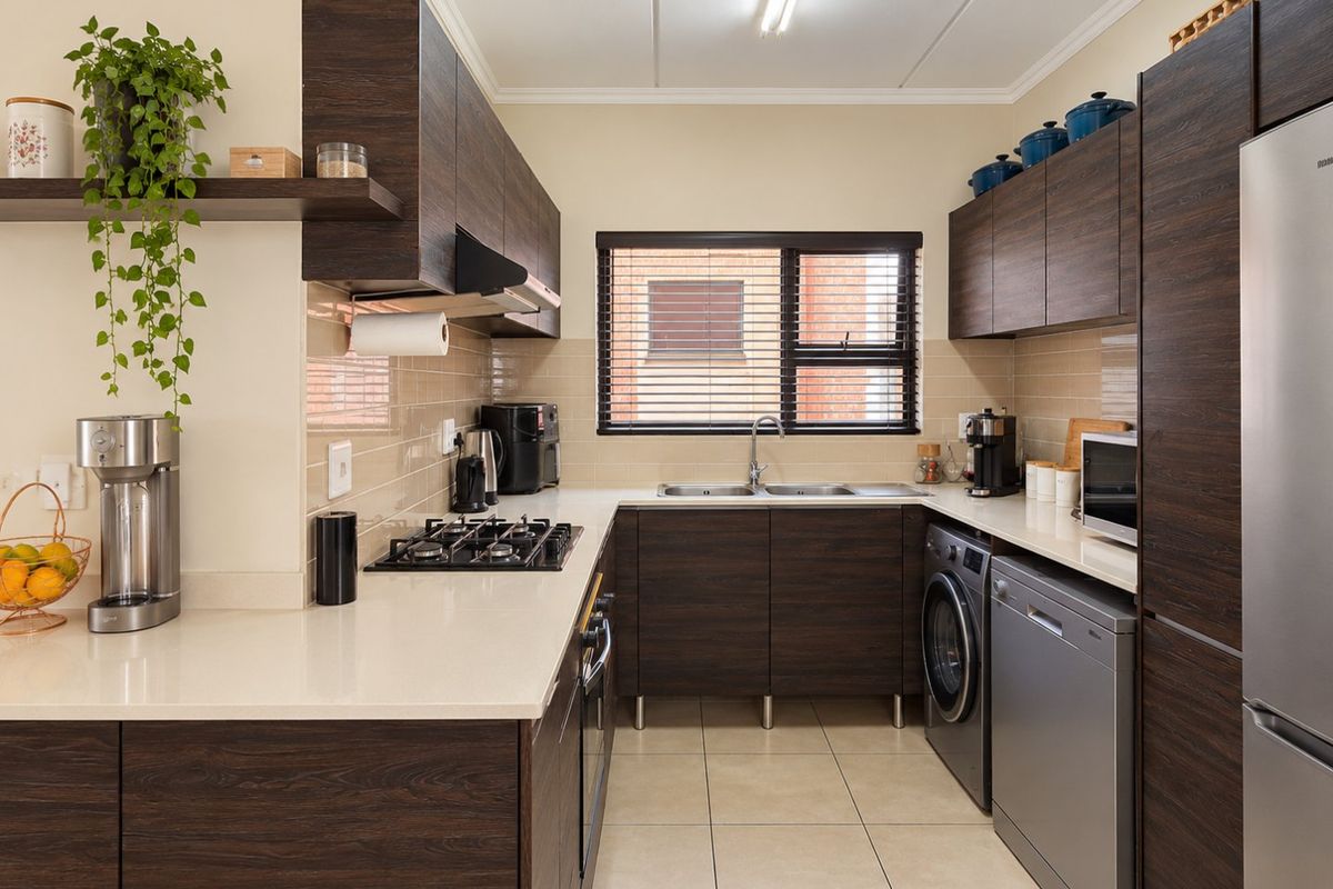 A well-maintained kitchen featuring dark wood cabinetry, stone countertops, a gas hob, built-in oven, and integrated space for laundry and dishwashing appliances.