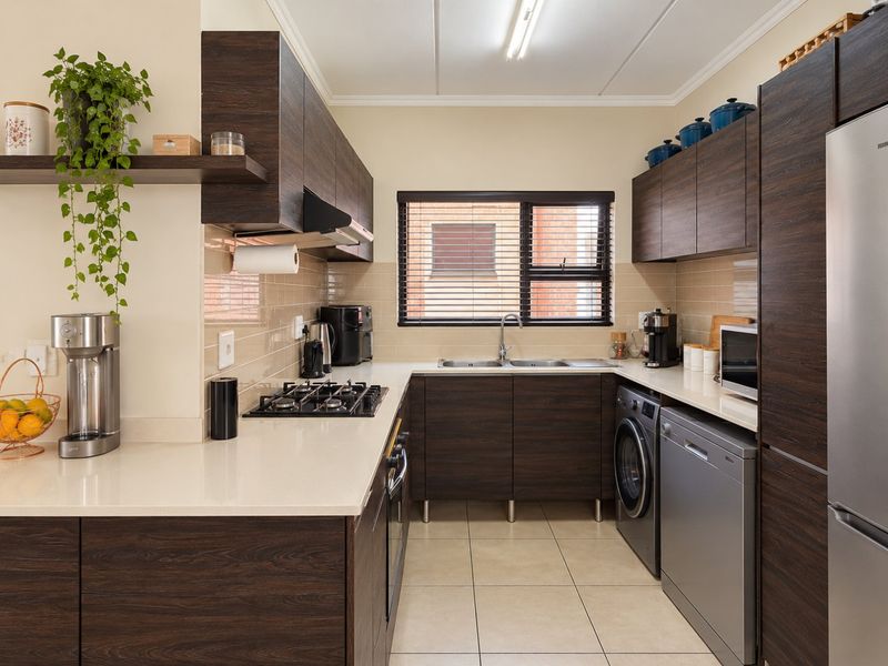 A well-maintained kitchen featuring dark wood cabinetry, stone countertops, a gas hob, built-in oven, and integrated space for laundry and dishwashing appliances.