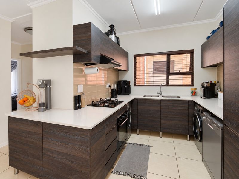 Modern kitchen featuring dark wood cabinetry, stone countertops, gas hob, built-in oven, and integrated space for laundry appliances.
