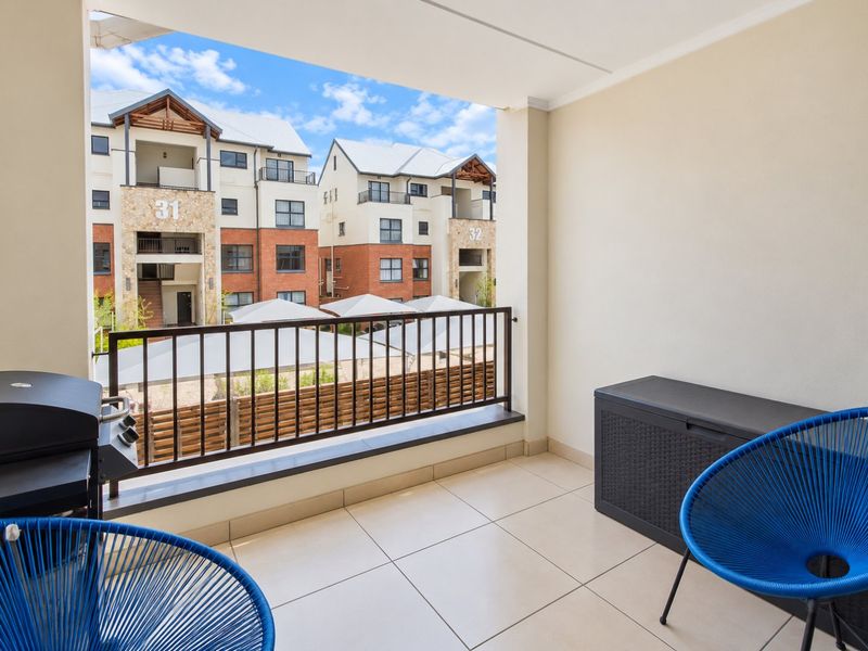 A covered balcony featuring tiled flooring and a metal balustrade, offering an outdoor space with views of the surrounding apartment complex.