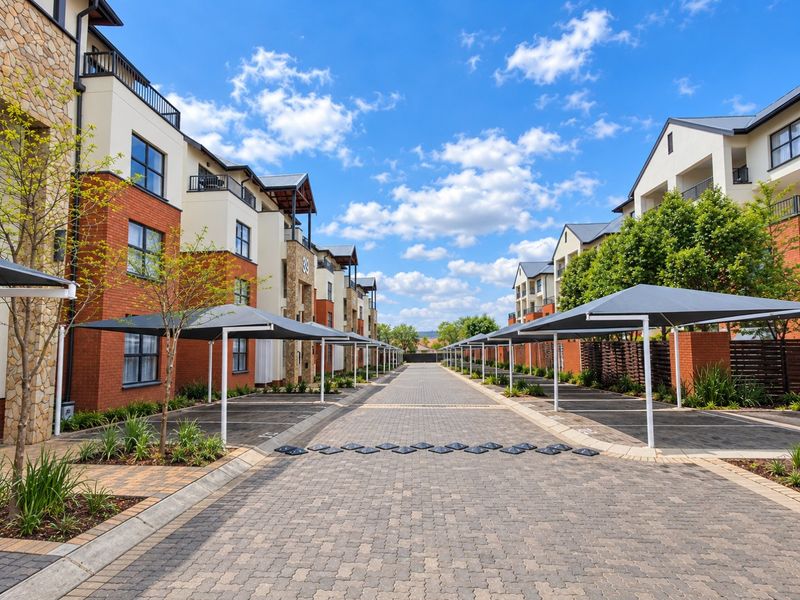 A well-maintained apartment complex exterior featuring a paved driveway, covered parking bays, and modern brick and stone architectural finishes.