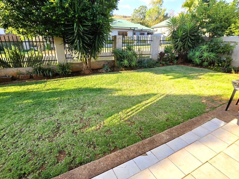 A private rear garden featuring a well-maintained lawn, perimeter metal fencing, and a tiled patio area suitable for outdoor relaxation.