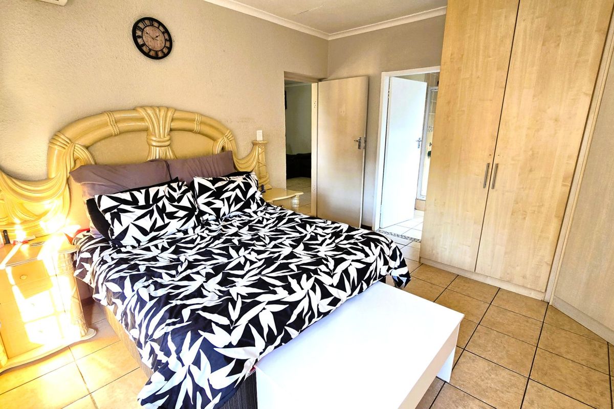 A bedroom featuring built-in wooden cupboards and tiled flooring, with direct access to an adjoining room.