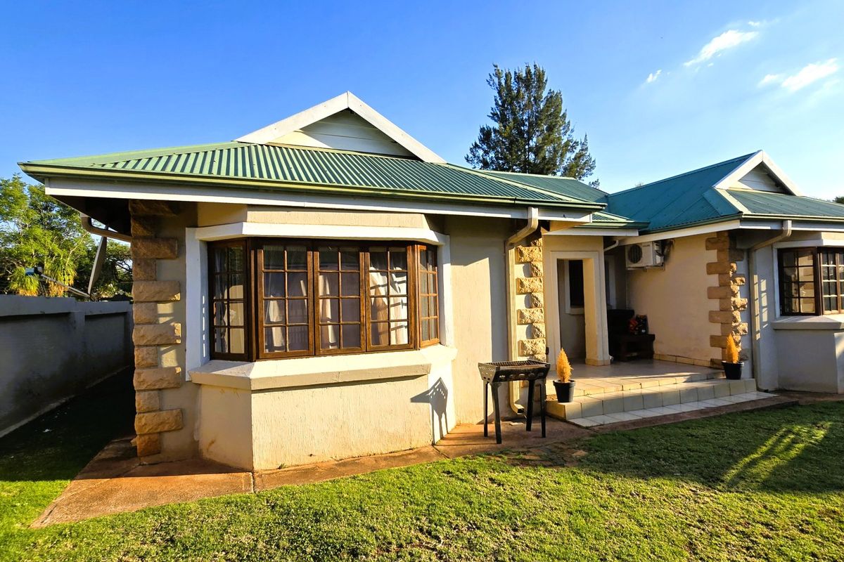 Rear view of a house featuring a green corrugated metal roof, stone corner detailing, a bay window, and a small covered patio area.