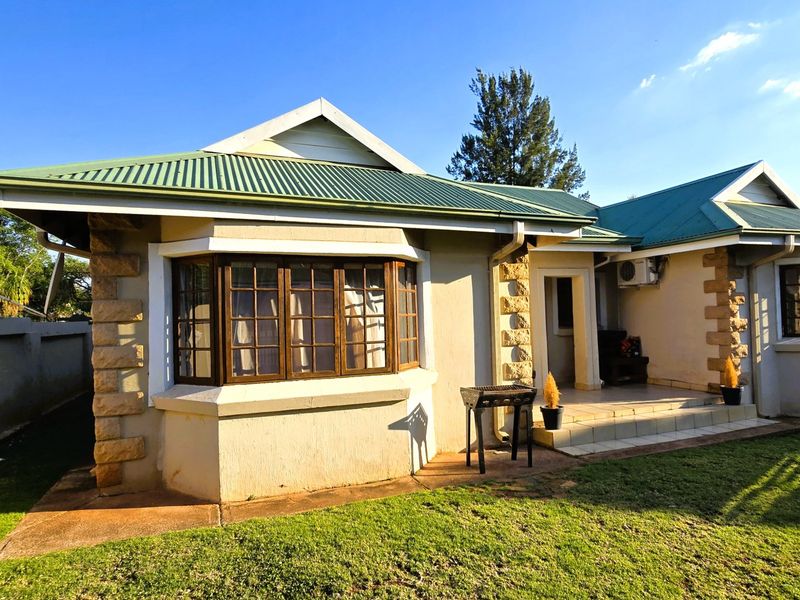 Rear view of a house featuring a green corrugated metal roof, stone corner detailing, a bay window, and a small covered patio area.