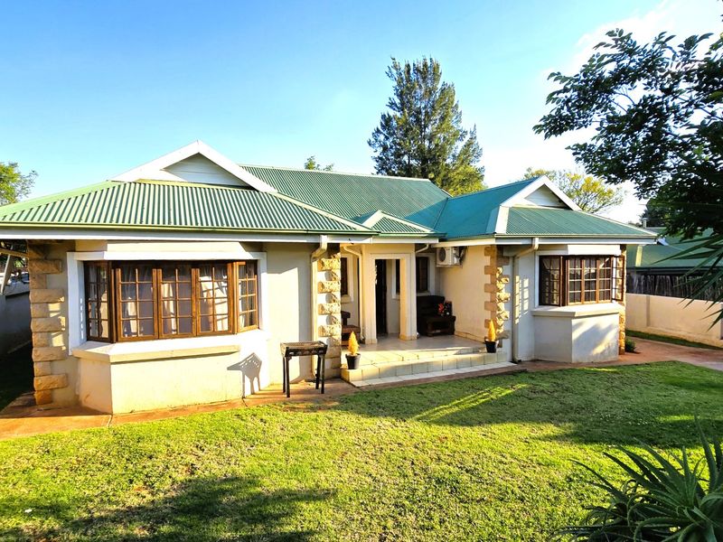 A charming single-story house featuring a green corrugated metal roof, stone-clad accents, and classic bay windows set within a well-maintained garden.