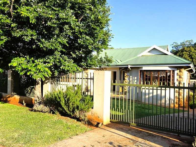 Front view of a residential house featuring a green corrugated metal roof, stone accents, and secure metal perimeter fencing with a gated driveway.