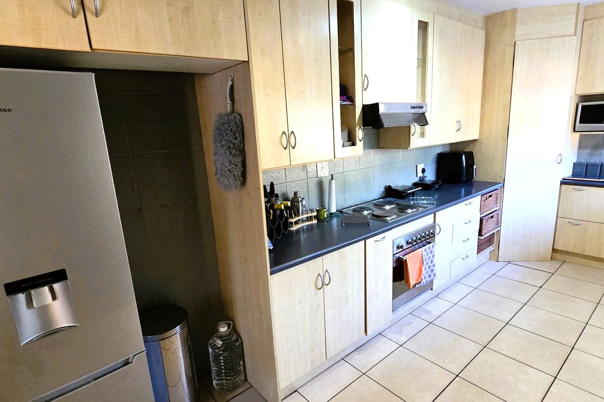 A functional kitchen featuring light wood-finish cabinetry, dark laminate countertops, integrated appliances, and tiled flooring with a practical layout.