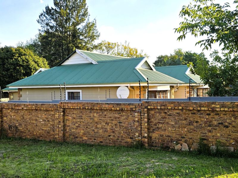A view of the property exterior featuring a brick boundary wall with electric fencing and a green corrugated metal roof.