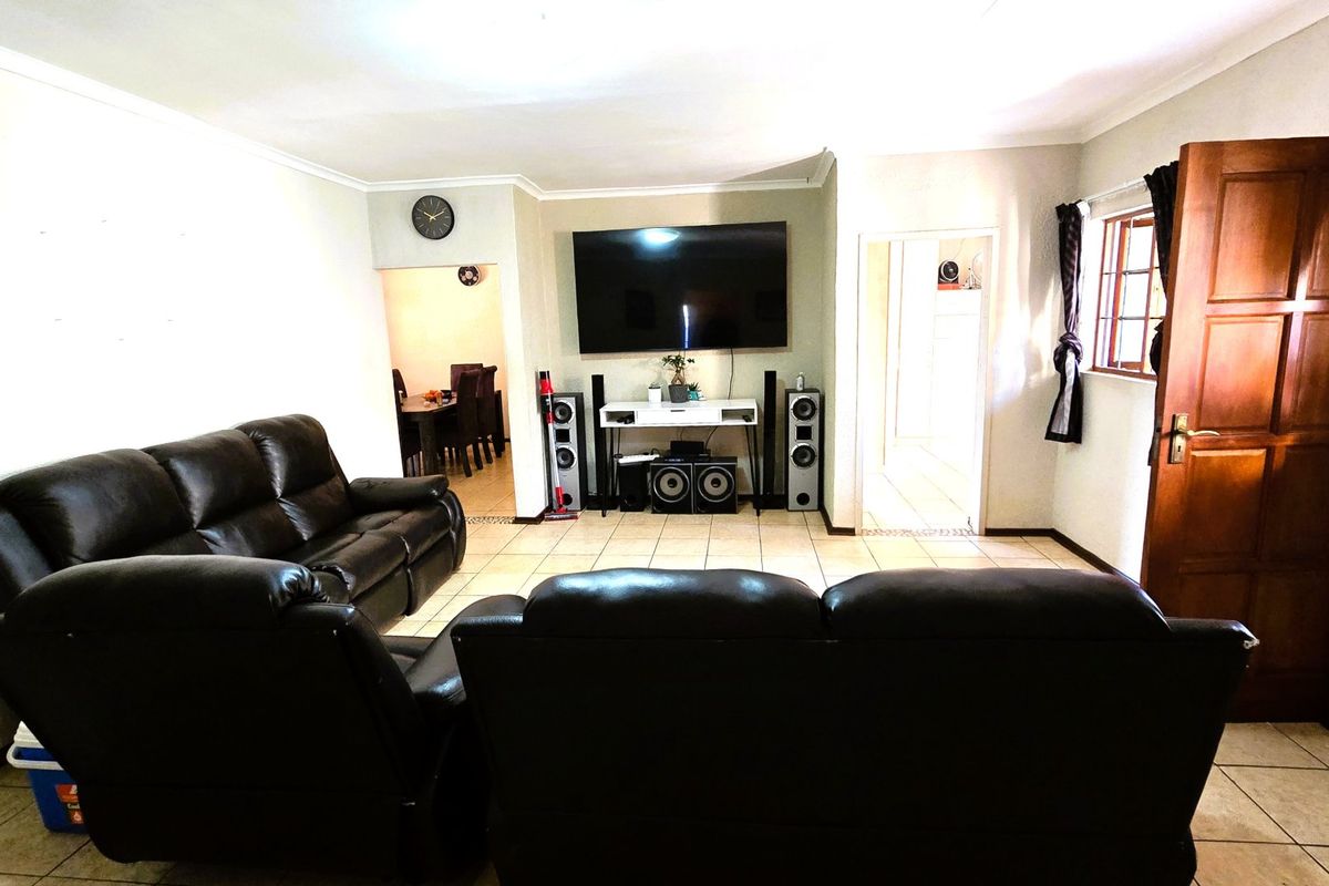 A spacious living room featuring tiled flooring, coved cornicing, and direct access to adjacent dining and hallway areas.