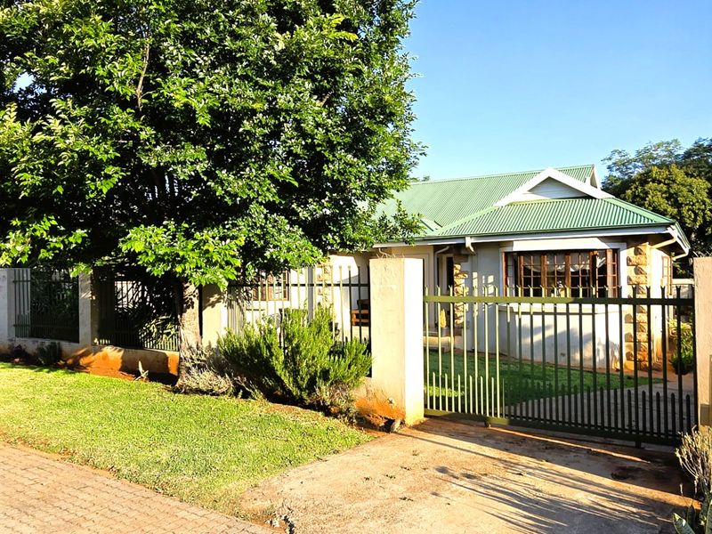 Front view of a residential property featuring a corrugated metal roof, stone accents, and a secure gated entrance with a paved driveway.