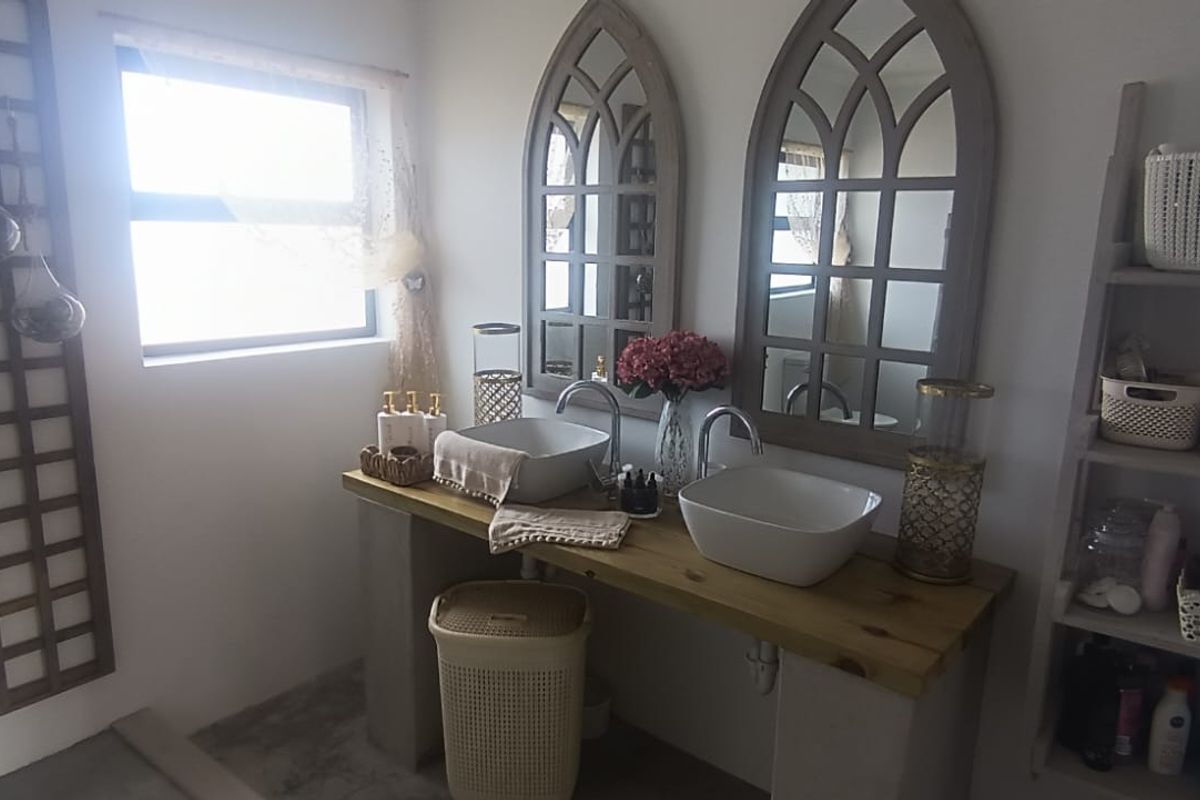 A bathroom featuring a double vanity with vessel sinks, chrome faucets, a timber countertop, and decorative arched mirrors.