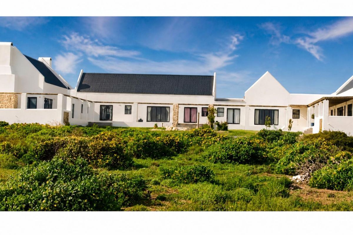 Rear view of a white-walled house with a dark metal pitched roof, featuring stone accents and a natural garden landscape.