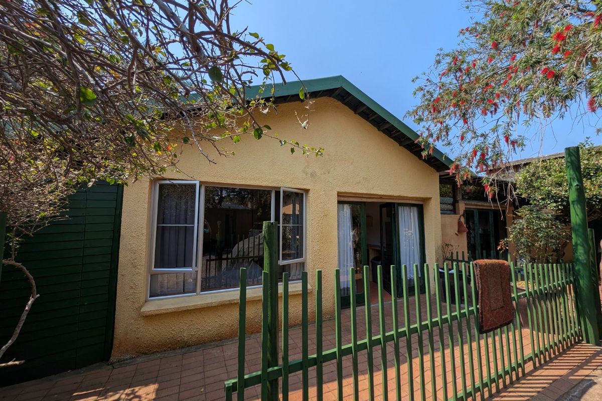 Rear exterior view of the apartment featuring a paved patio area, metal security fencing, and aluminium-framed windows and sliding doors.