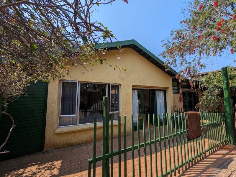 Rear exterior view of the apartment featuring a paved patio area, metal security fencing, and aluminium-framed windows and sliding doors.