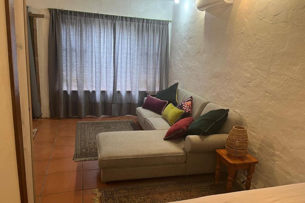 A cozy living room featuring textured walls, terracotta floor tiles, exposed ceiling beams, and a wall-mounted split-system air conditioner.