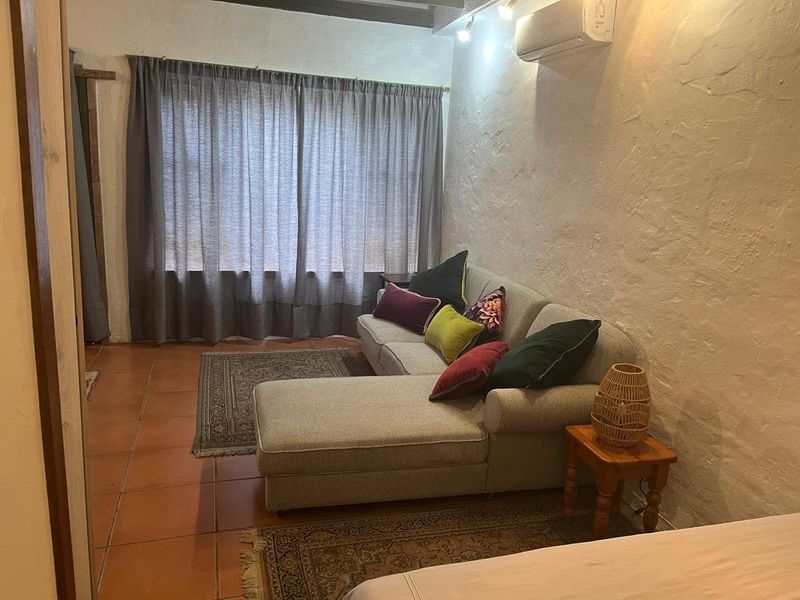 A cozy living room featuring textured walls, terracotta floor tiles, exposed ceiling beams, and a wall-mounted split-system air conditioner.