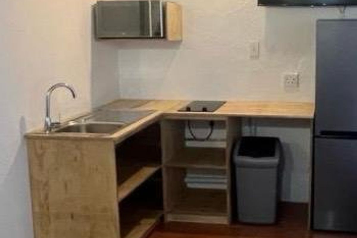 A compact kitchenette featuring a sink, built-in microwave, and cooktop with open wooden shelving and tiled flooring.