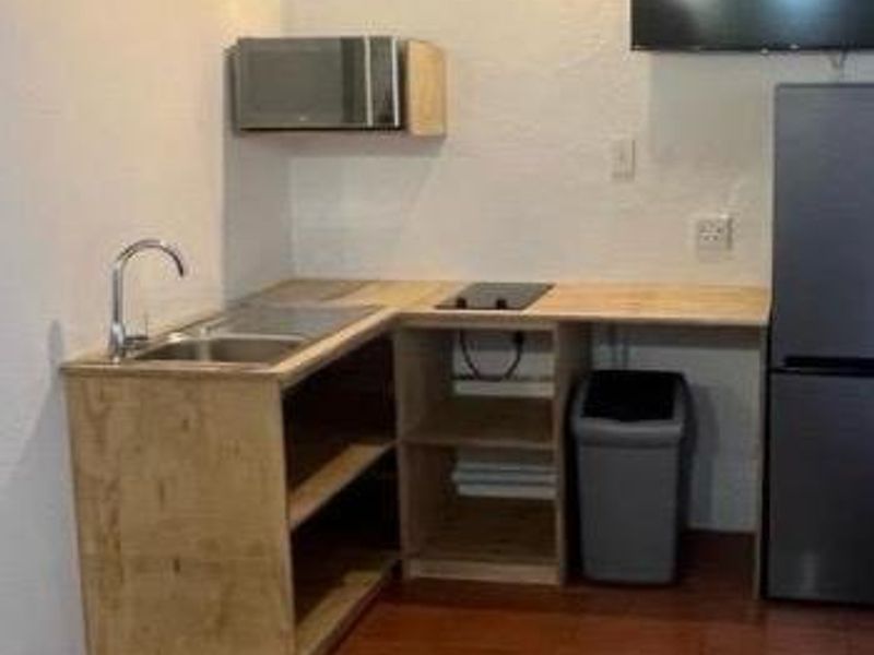 A compact kitchenette featuring a sink, built-in microwave, and cooktop with open wooden shelving and tiled flooring.