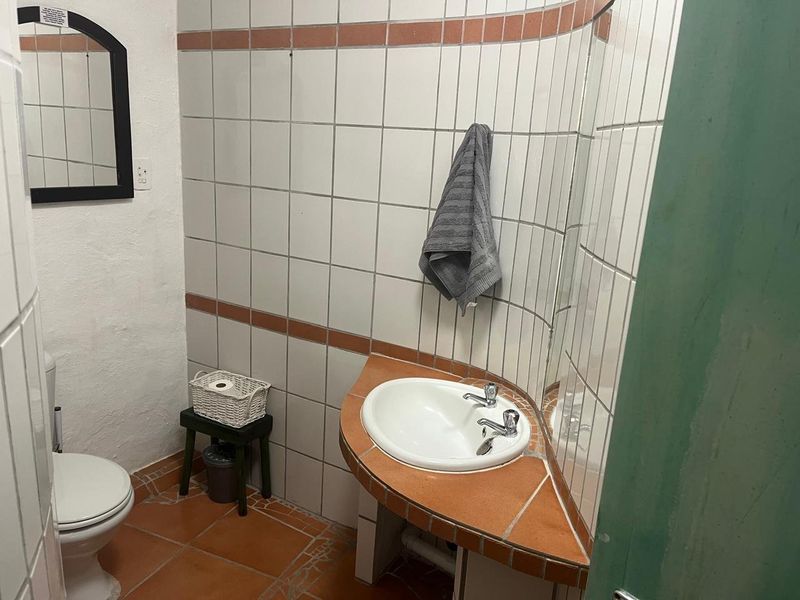 A compact bathroom featuring a built-in corner vanity with a ceramic basin, tiled walls, and terracotta-style floor tiles.