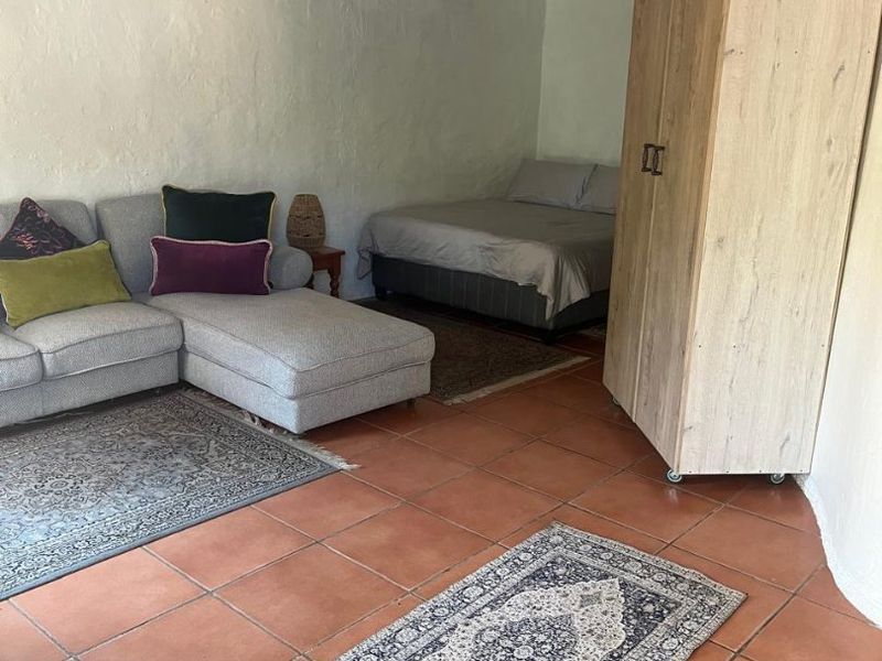 Open-plan living and sleeping area featuring terracotta floor tiles, exposed timber ceiling beams, and a wall-mounted air conditioning unit.