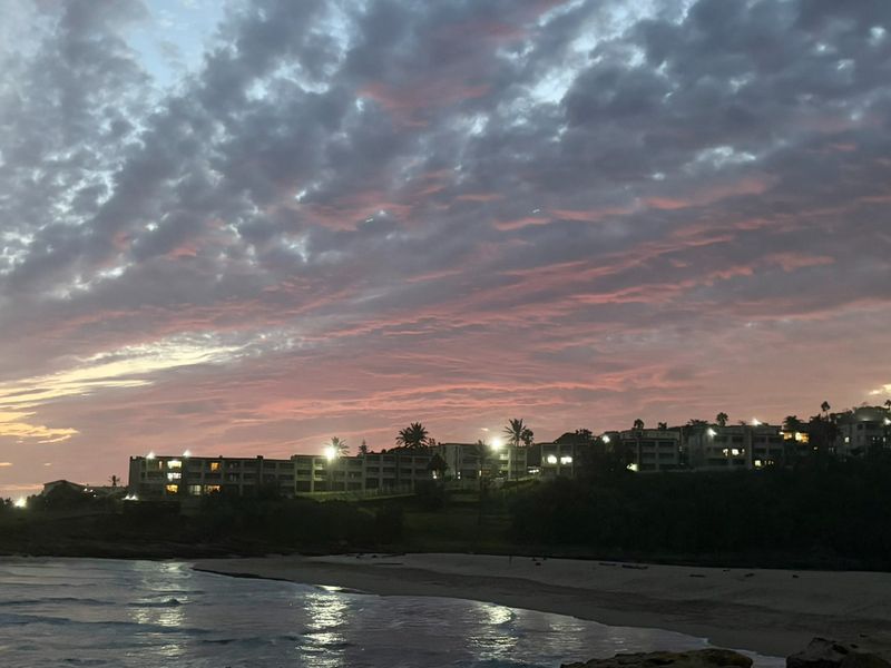 A scenic evening view of the coastline featuring the apartment complex illuminated against a dramatic sunset sky.