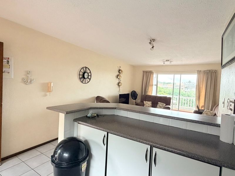Open plan living area featuring a breakfast bar, tiled flooring, and sliding glass doors leading to a balcony.