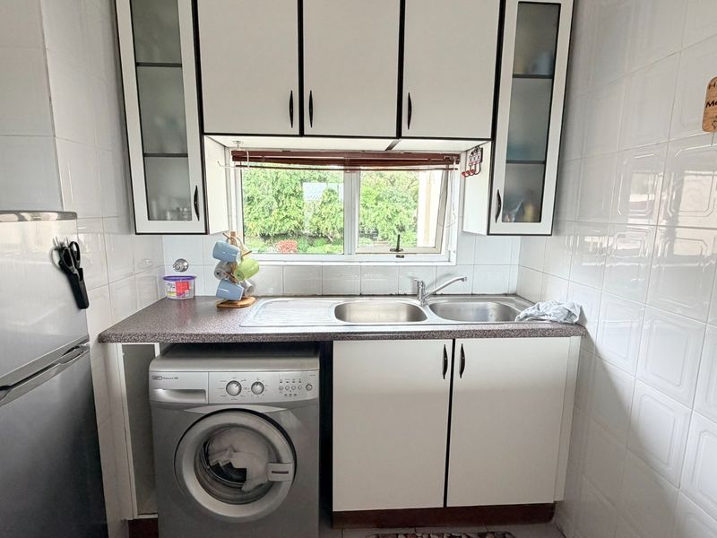 Compact kitchen featuring white cabinetry, laminate countertops, a double sink, and tiled wall finishes with a window overlooking the exterior.