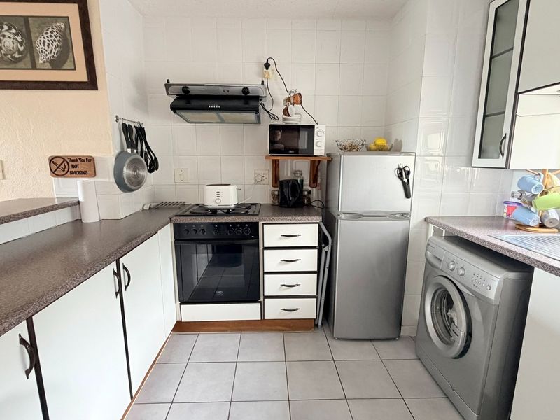 A functional kitchen featuring white cabinetry, laminate countertops, tiled backsplash, built-in oven with hob, extractor fan, and integrated laundry appliance space.