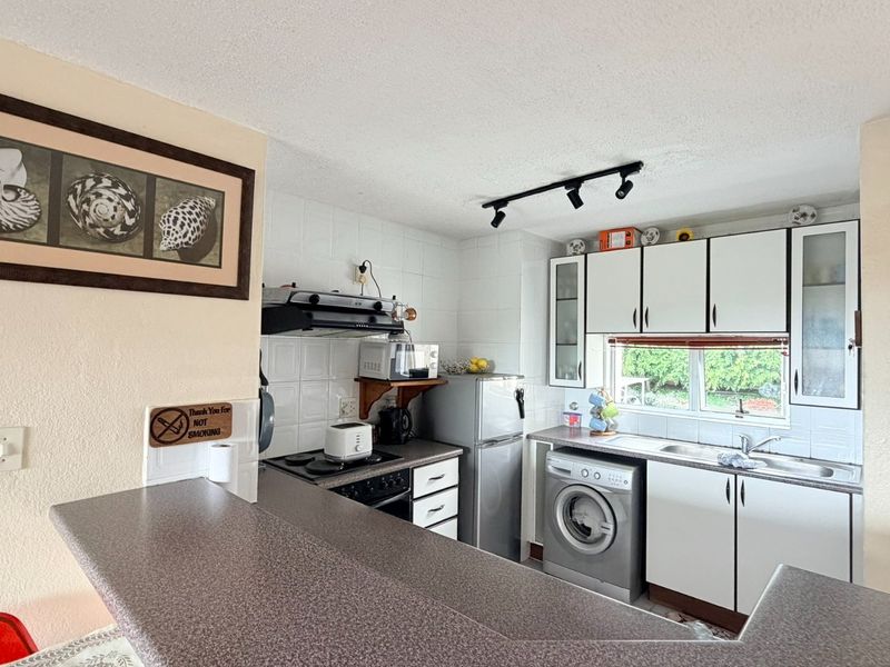 Functional kitchen featuring white cabinetry, laminate countertops, tiled backsplash, and integrated laundry plumbing, offering a practical layout for daily use.