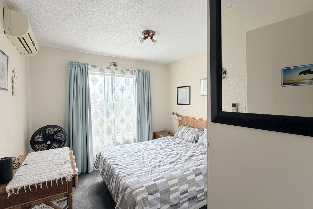 A functional bedroom featuring carpeted flooring, a split-system air conditioner, and a window with curtains, providing a comfortable and well-lit sleeping space.