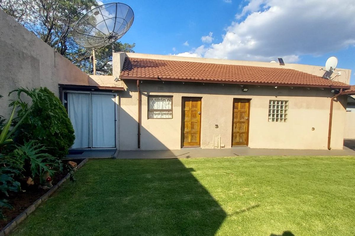 Rear view of the property featuring a lawn, boundary wall, tiled roof, and multiple access doors with security gates.