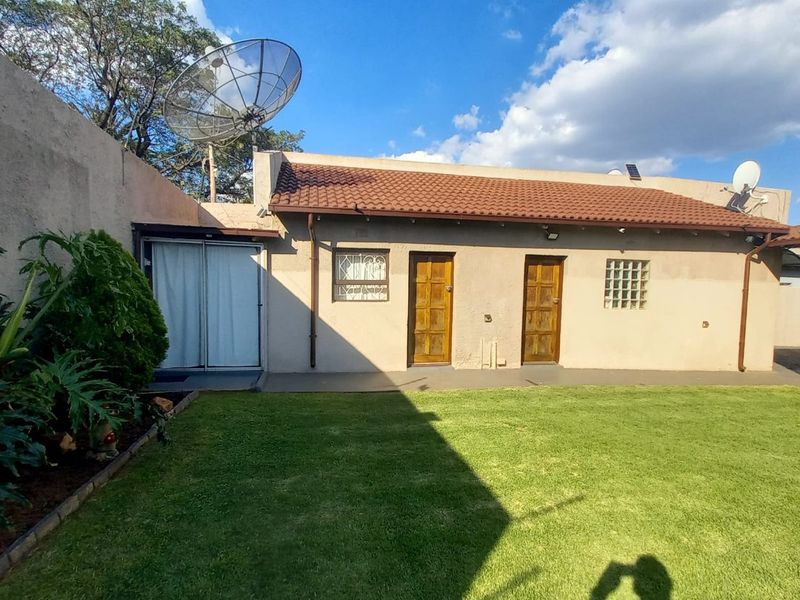 Rear view of the property featuring a lawn, boundary wall, tiled roof, and multiple access doors with security gates.