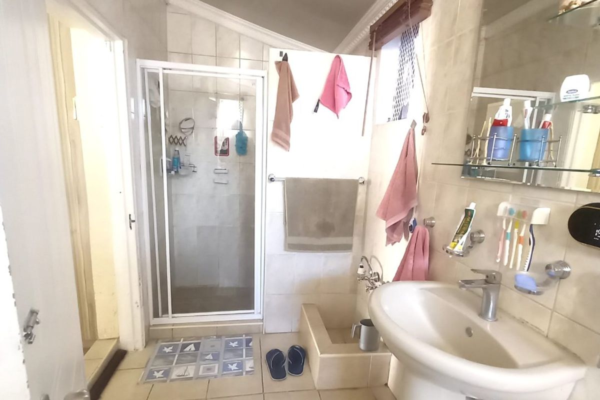 A functional bathroom featuring a pedestal basin, a glass-enclosed shower, and neutral wall and floor tiling.