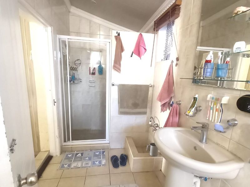 A functional bathroom featuring a pedestal basin, a glass-enclosed shower, and neutral wall and floor tiling.