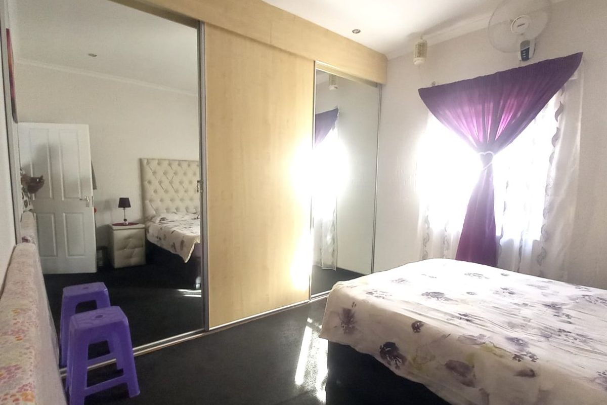 A bedroom featuring built-in sliding door wardrobes with mirrored panels, recessed ceiling lighting, and a wall-mounted fan.