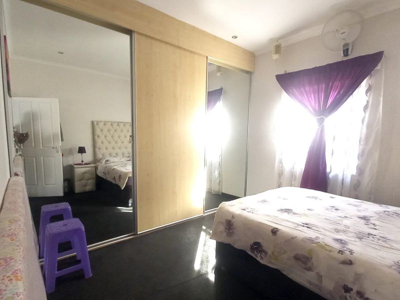 A bedroom featuring built-in sliding door wardrobes with mirrored panels, recessed ceiling lighting, and a wall-mounted fan.
